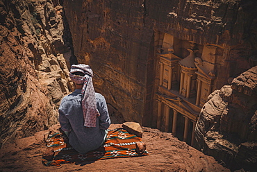 Tourist with turban sits on carpet and looks from above into the canyon Siq, Pharaoh's treasure house beaten into rock, facade of the treasure house Al-Khazneh, Khazne Faraun, mausoleum in the Nabataean city Petra, near Wadi Musa, Jordan, Asia