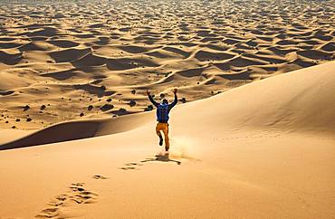 Young man walking down a sand dune, dune landscape Erg Chebbi, Merzouga, Sahara, Morocco, Africa