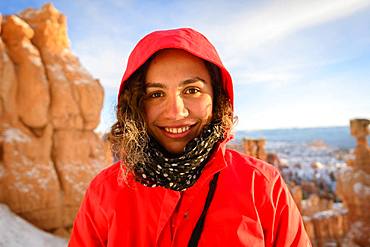 Portrait of a pretty young woman in winter clothes in front of rock needles, Winter, Rim Trail, Bryce Canyon National Park, Utah, USA, North America