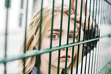 Young blonde woman, teenager looking thoughtfully through a grid, North Rhine-Westphalia, Germany, Europe