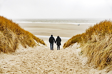 In bad weather a couple walks through the dunes to the beach, Langeoog, East Frisia, Niedersachsen, Germany, Europe