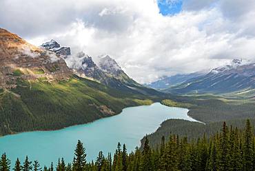 Clouds hanging in mountain peaks, turquoise glacial lake surrounded by forest, Peyto Lake, Rocky Mountains, Banff National Park, Alberta Province, Canada, North America