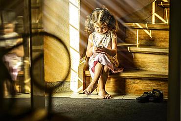 Girl, 3 years old, sitting on stairs listening to music with headphones, Germany, Europe