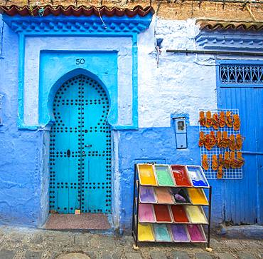 Blue entrance door with blue house facade, next to it color pigments and leather sandals for sale, Medina of Chefchaouen, Chaouen, Tanger-Tetouan, Morocco, Africa