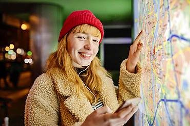 Girl, teenager, with smartphone in her hand standing at night in the city in front of city map, Cologne, North Rhine-Westphalia, Germany, Europe