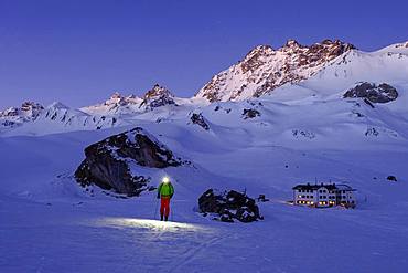 Ski tourer with headlamp in front of Heidelberger Huette, dawn, Silvretta, Graubuenden, Switzerland, Europe