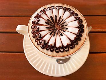 Latte Art, Cappuccino with artfully decorated milk foam in the cup on wooden table, Bangkok