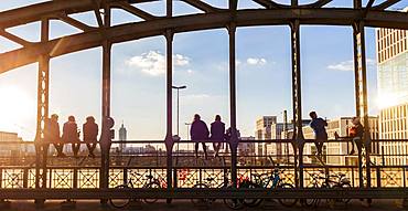 Young people sitting on the balustrade of the Hackerbruecke bridge over the railway tracks and looking into the distance, back light, Munich, Upper Bavaria, Bavaria, Germany, Europe