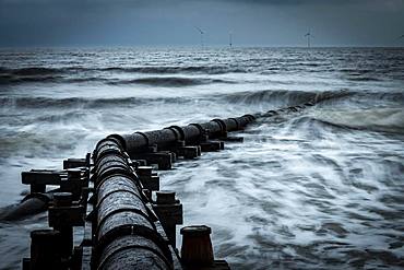 Corroded iron pipe, sewage pipe in the sea surf under a dark sky, Blyth, Northumberland, Great Britain