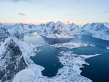 Snow-covered mountains at the fjord with place Reine, sunrise, drone shot, Lofoten, Norway, Europe