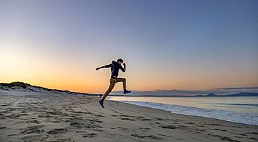 Young man jumps into the air, beach Waipu Beach at sunset, Waipu Cove, Northland, New Zealand, Oceania