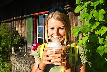 Young female hiker drinks buttermilk at the Kraftalm, Hohe Salve, Itter, Kitzbuehel Alps, Tyrol, Austria, Europe