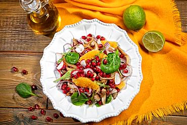 Served salad on a porcelain plate with orange slices, pomegranate, rocket and oyster mushrooms, on a wooden desk and fabric, food, Russia, Europe