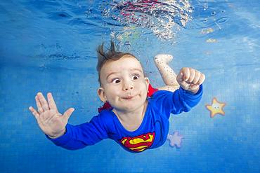 Little boy in a superman costume dives underwater in the pool, front view, Ukraine, Europe