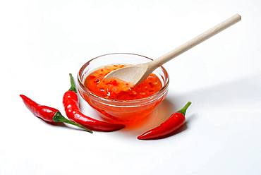 Chilli sauce in small bowl with cooking spoon and chilli peppers, Germany, Europe