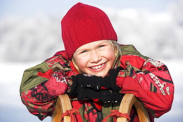 Little girl leaning on a sledge and laughing, portrait, Upper Austria, Austria, Europe