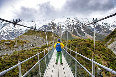 Hiker crosses suspension bridge over Hooker River, Hooker Valley, Mount Cook National Park, Canterbury, New Zealand, Oceania