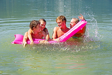 Four teenagers on an air mattress in water have fun bathing, 18 years, Mondsee, Upper Austria, Austria, Europe