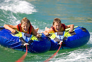 Two children, teenagers rafting with water tyres in a lake, Lake Mondsee, Upper Austria, Austria, Europe