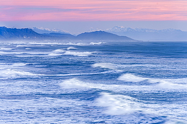 Leaking waves of the ocean under a pink evening sky with mountain silhouette, Punakaiki, Paparoa National Park, West Coast Region, New Zealand, Oceania