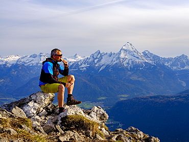 Mountaineer with a snack at the summit Rauher Kopf, Berchtesgadener Alps, behind Watzmann, Bischofswiesen, Berchtesgadener Land, Upper Bavaria, Bavaria, Germany, Europe