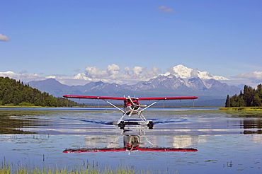 Seaplane Beaver de Havilland lands on a lake off snow-covered mountain Denali, Alaska, USA, North America