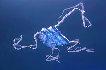 Close-up, discarded used medical face mask slowly drifts on the water surface (underwater view) Becici, Budva Municipality, Montenegro, Europe