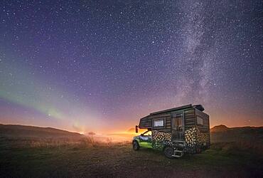 Night shot of a painted camper van under the Milky Way with northern lights, Gimsoy, Lofoten, Nordland, Norway, Europe