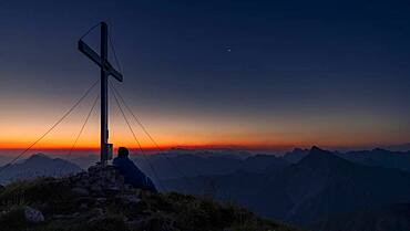 Cross of the Kreuzspitze at sunrise with mountaineer at the summit, in the background the Lechtal Alps, Elmen, Lechtal Alps, Ausserfern, Tyrol, Austria, Europe