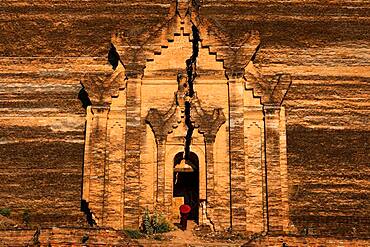 Buddhist monk stands with red umbrella in the entrance of Mingun Pagoda, Mingun, Myanmar, Asia