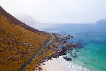 Drone shot, road between a mountain and in front of a fine sandy beach, Haukland beach, Lofoten, Norway, Europe