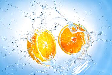 Two halves of oranges fall into water with splashes of water, light blue background