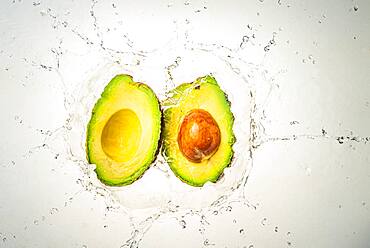 Two halves of avocado splashing into clear water, light background