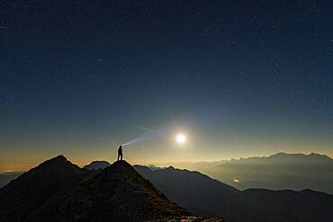 Mountaineer on summit ridge with full moon and starry sky, in the background Ammergau Alps, Reutte, Ammergau Alps, Tyrol, Austria, Europe