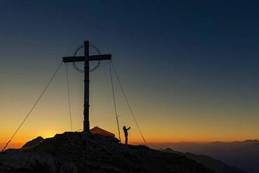 Sunrise over Ammergau mountains, in the foreground summit cross of the Geierkopf with mountaineer and tent, Reutte, Ammergau Alps, Tyrol, Austria, Europe