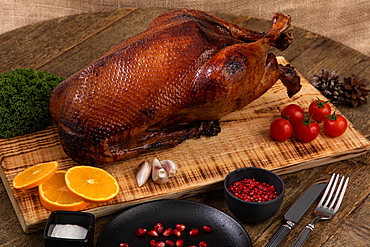 Crispy, roast goose on wooden board with vegetables and cutlery placed around