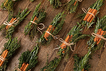 Cinnamon sticks tied together with rosemary and thyme, several bunches of herbs next to each other, on wooden underground