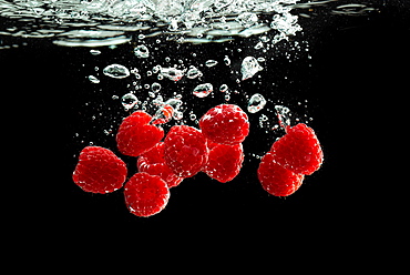 Raspberries fall into the water, black background