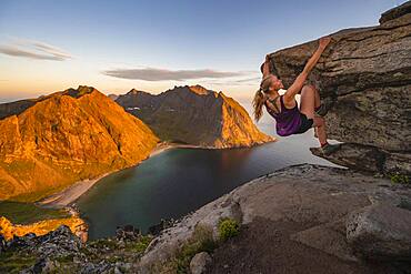 Evening atmosphere, Young woman bouldering, Climbing, Peak of Ryten, Sea, Kvalvika beach and mountains, Fredvang, Lofoten, Nordland, Norway, Europe