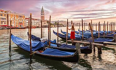 Woman with red dress looking at Venice, evening mood, sunset at the Grand Canal, gondolas at the pier, Campanile bell tower, Venice, Veneto region, Italy, Europe