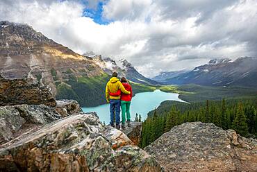 Couple hugging, looking into the distance, view of turquoise glacial lake surrounded by forest, Peyto Lake, Rocky Mountains, Banff National Park, Alberta Province, Canada, North America