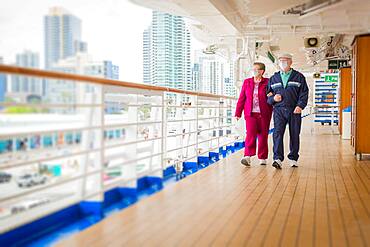 Senior couple walk along passenger cruise ship Ddck wearing face masks, USA, North America