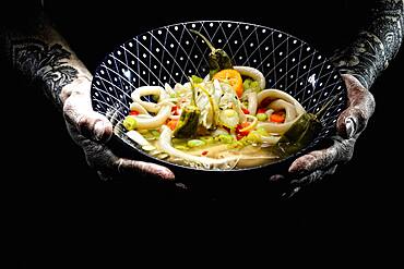 Tattooed hands hold plate with udon bowl, japanese noodle soup