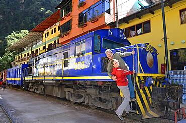 Two tourists at the locomotive of the Perurail in the station, Aguas Calientes, Machu Picchu, Urubamba Province, Peru, South America