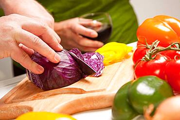 Man slicing vegetables on cutting board while woman enjoys a glass of red wine