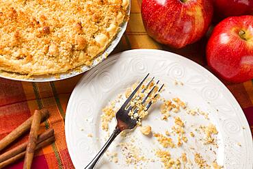 Overhead abstract of apple pie, empty plate with remaining crumbs and fork