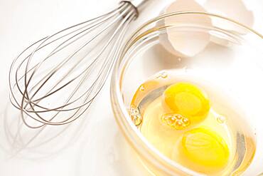 Hand mixer with eggs in a glass bowl on a reflective white background