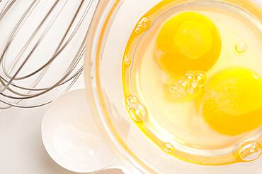 Hand mixer with eggs in a glass bowl on a reflective white background