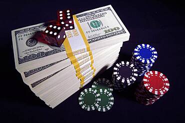 Stack of ten thousand dollar piles of one hundred dollar bills, red dice & poker chips on a black background