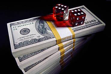 Stack of ten thousand dollar piles of one hundred dollar bills & dice on a black background